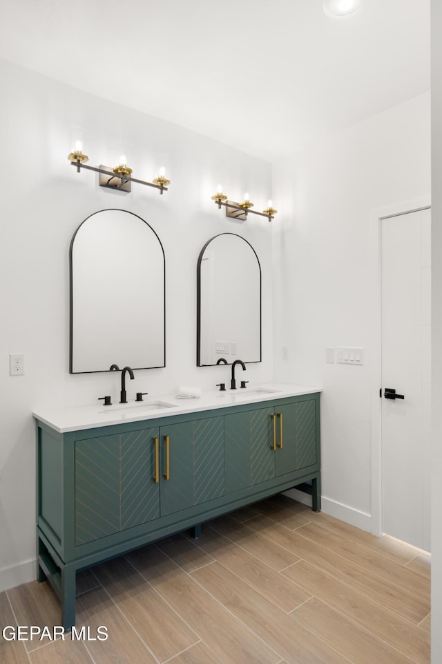 bathroom with a sink, baseboards, wood finish floors, and double vanity