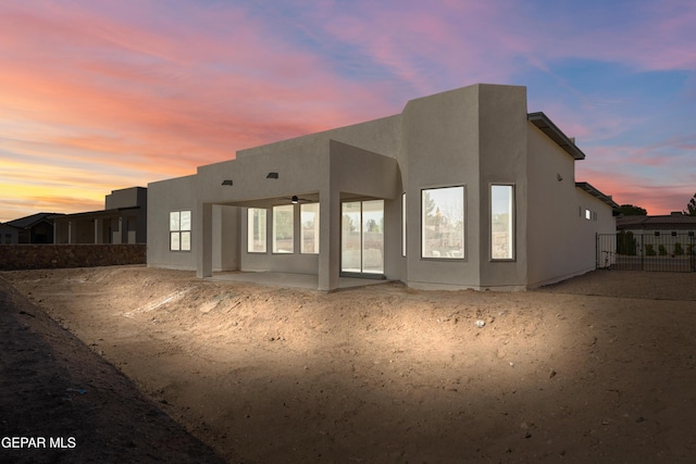 back of property at dusk featuring a patio, fence, and stucco siding