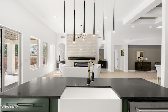 kitchen with dark countertops, open floor plan, a fireplace, a high ceiling, and a sink