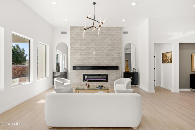 living area with a notable chandelier, visible vents, light wood-style flooring, and a tiled fireplace