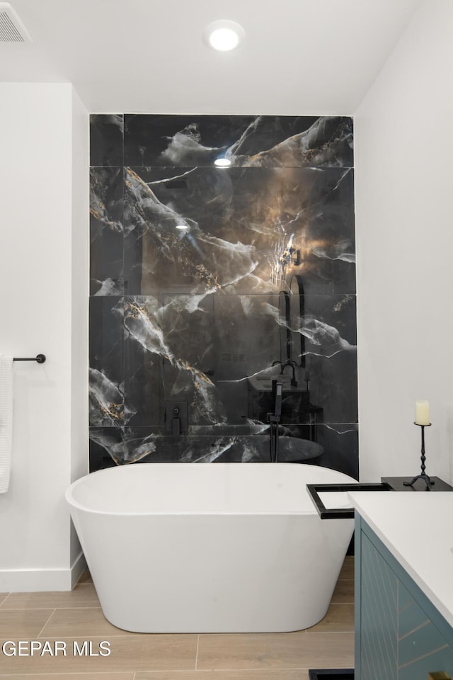 full bath with a soaking tub, visible vents, vanity, and wood finish floors