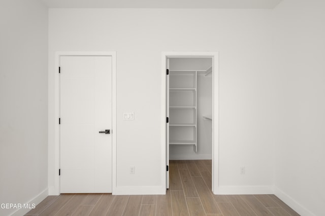 unfurnished bedroom featuring a walk in closet, baseboards, and wood tiled floor