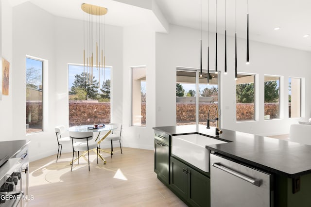 kitchen with an island with sink, a sink, stainless steel dishwasher, dark countertops, and light wood finished floors