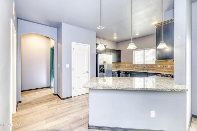 kitchen with stainless steel appliances, arched walkways, light wood-style floors, a peninsula, and light stone countertops