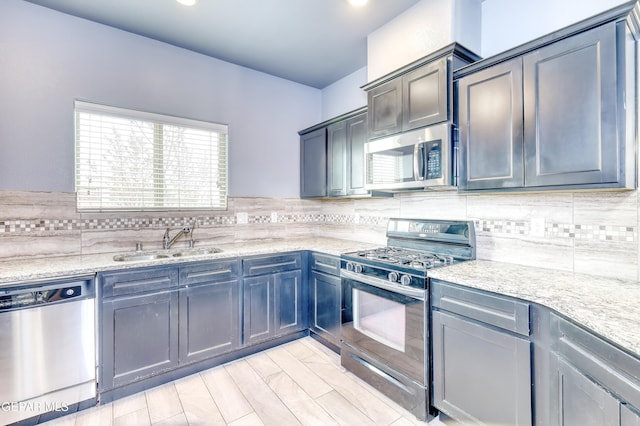 kitchen with tasteful backsplash, stainless steel appliances, light stone counters, and a sink