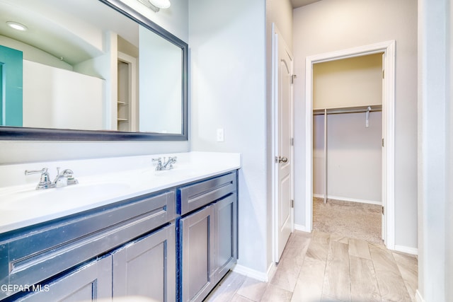 bathroom with double vanity, a spacious closet, baseboards, and a sink