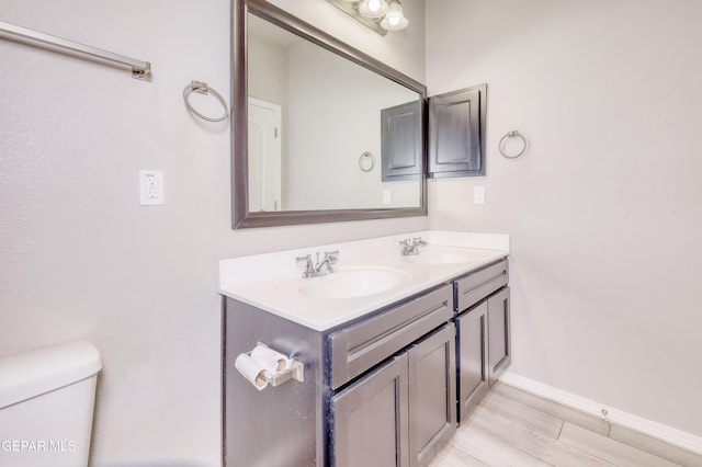 bathroom featuring double vanity, toilet, baseboards, and a sink