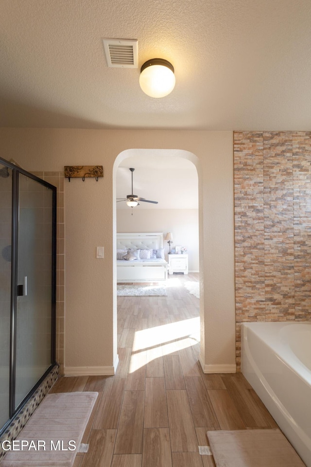 bathroom featuring wood finished floors, visible vents, a stall shower, ceiling fan, and a textured ceiling