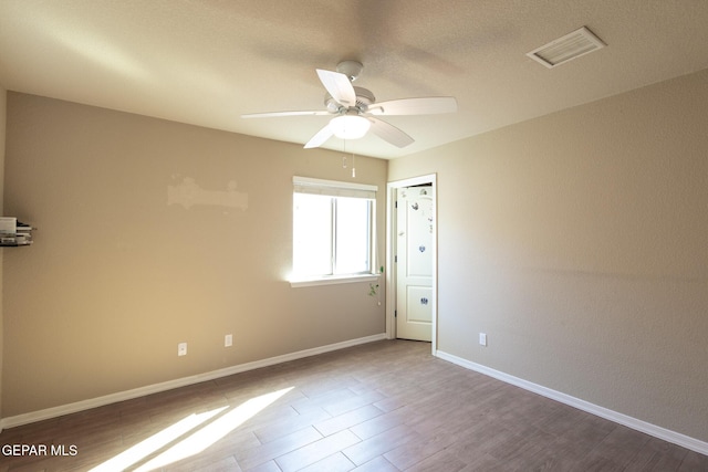 spare room featuring wood finished floors, baseboards, visible vents, and ceiling fan