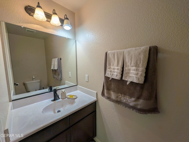 bathroom with vanity, toilet, a textured wall, and visible vents