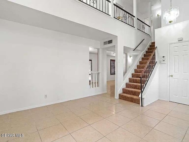 staircase featuring tile patterned floors, baseboards, visible vents, and a towering ceiling