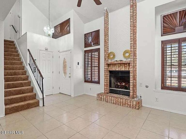 entrance foyer with tile patterned floors, ceiling fan with notable chandelier, high vaulted ceiling, and stairs