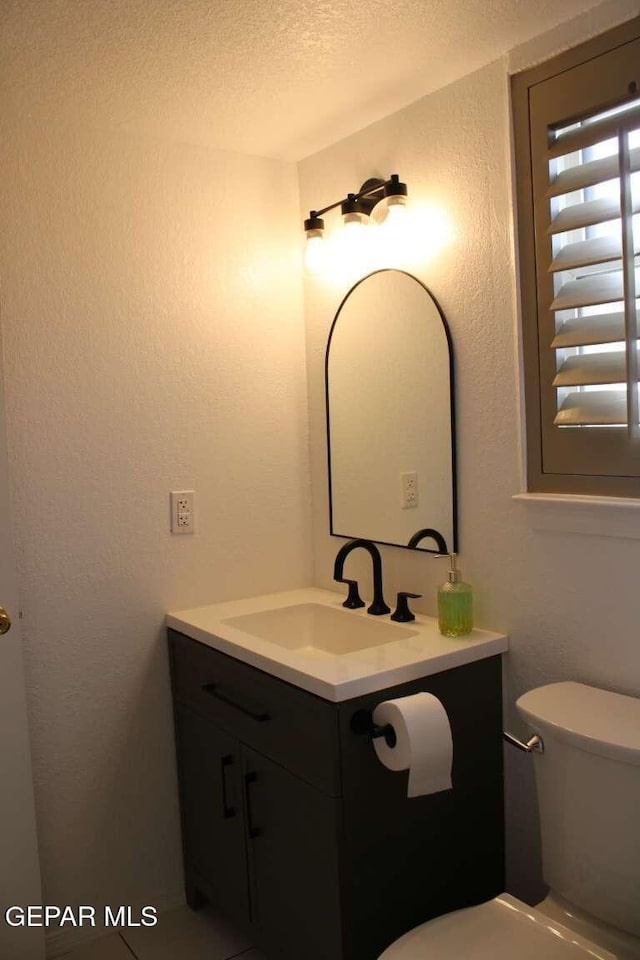 bathroom with a textured ceiling, toilet, vanity, and a textured wall