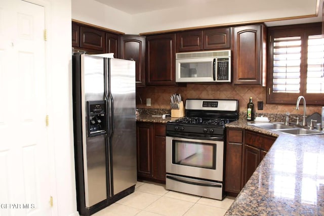 kitchen with a sink, backsplash, stainless steel appliances, dark brown cabinetry, and light tile patterned flooring