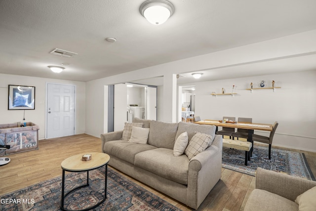 living area with visible vents, a textured ceiling, washer / dryer, and wood finished floors