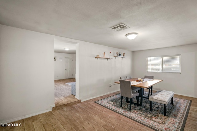 dining area featuring visible vents, baseboards, a textured ceiling, and wood finished floors