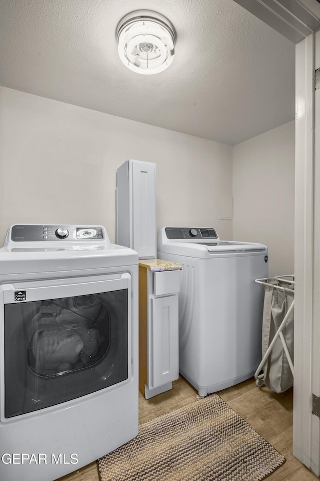 laundry area with a textured ceiling, laundry area, light wood-style flooring, and washing machine and clothes dryer