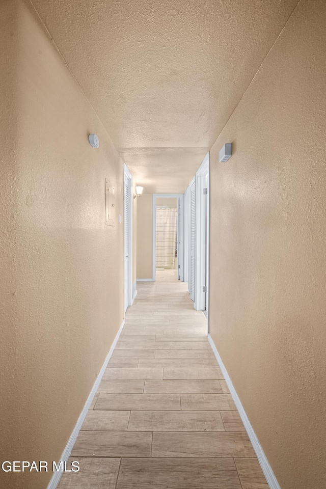 corridor with a textured ceiling, a textured wall, baseboards, and wood finish floors