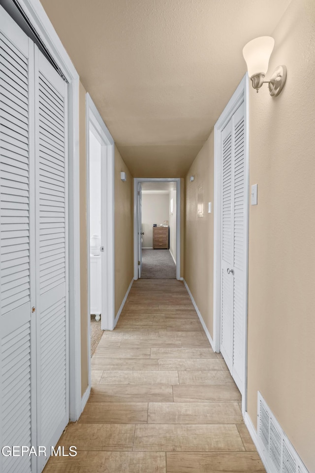 corridor with baseboards, visible vents, light wood finished floors, and a textured ceiling