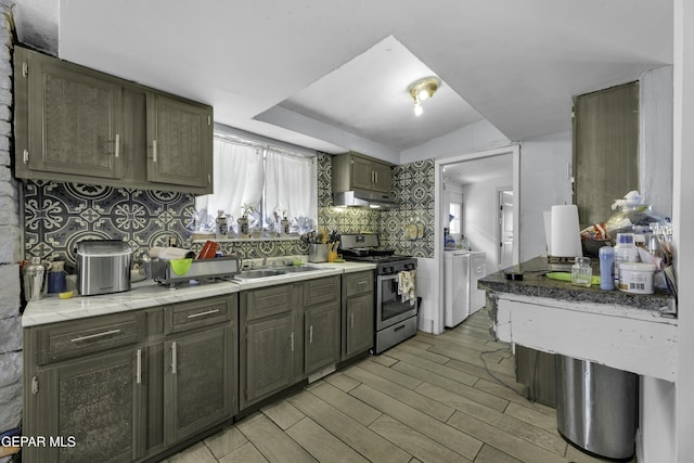 kitchen featuring stainless steel range with gas cooktop, a sink, under cabinet range hood, washer and dryer, and tasteful backsplash