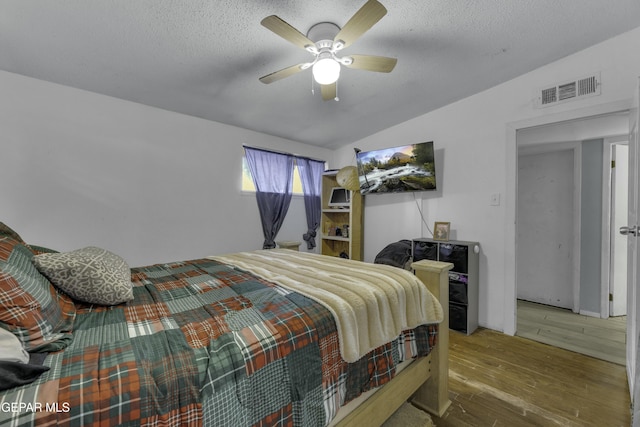 bedroom featuring visible vents, lofted ceiling, a textured ceiling, and wood finished floors