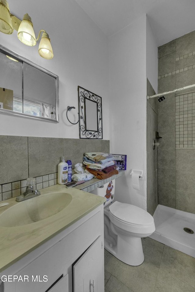 bathroom with toilet, tasteful backsplash, a tile shower, tile patterned flooring, and vanity