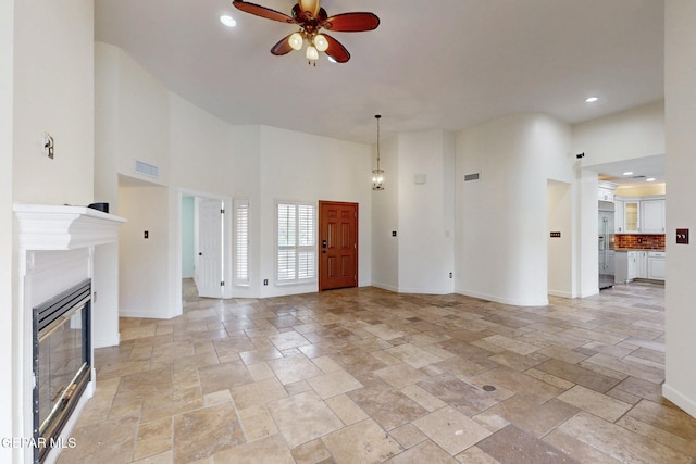 unfurnished living room with stone tile flooring, a ceiling fan, and a towering ceiling