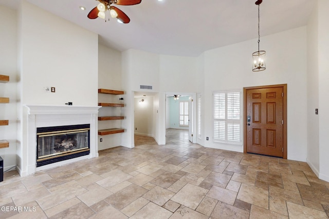 entryway with stone tile flooring, a glass covered fireplace, a towering ceiling, and ceiling fan with notable chandelier