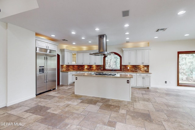 kitchen with visible vents, stainless steel built in refrigerator, gas cooktop, backsplash, and island range hood