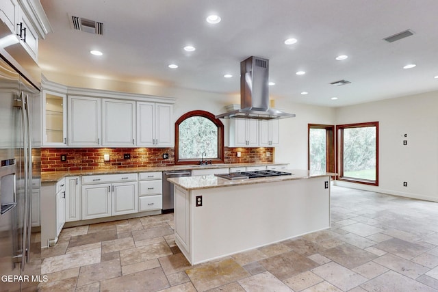 kitchen featuring stainless steel dishwasher, island exhaust hood, visible vents, and stone tile flooring