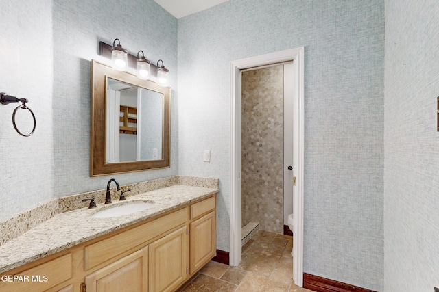 bathroom featuring vanity, stone finish floor, toilet, and wallpapered walls