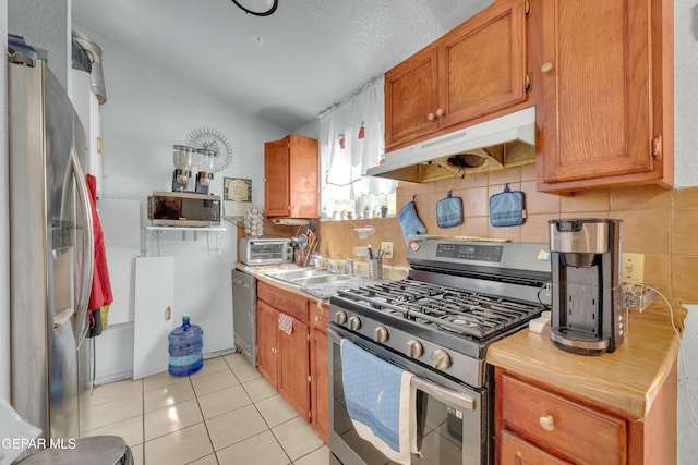 kitchen featuring backsplash, under cabinet range hood, light tile patterned floors, appliances with stainless steel finishes, and brown cabinetry