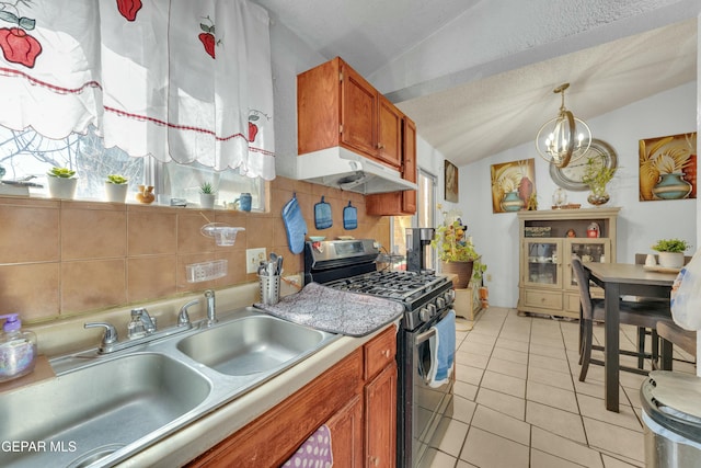 kitchen featuring stainless steel gas range oven, under cabinet range hood, a sink, lofted ceiling, and a chandelier