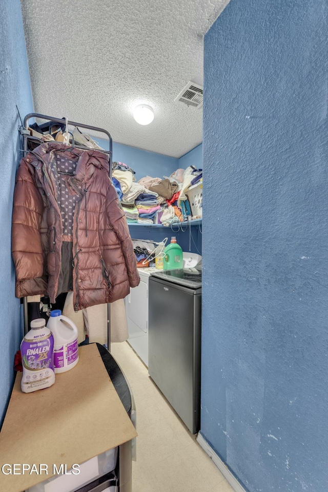 clothes washing area featuring visible vents, a textured ceiling, separate washer and dryer, laundry area, and a textured wall