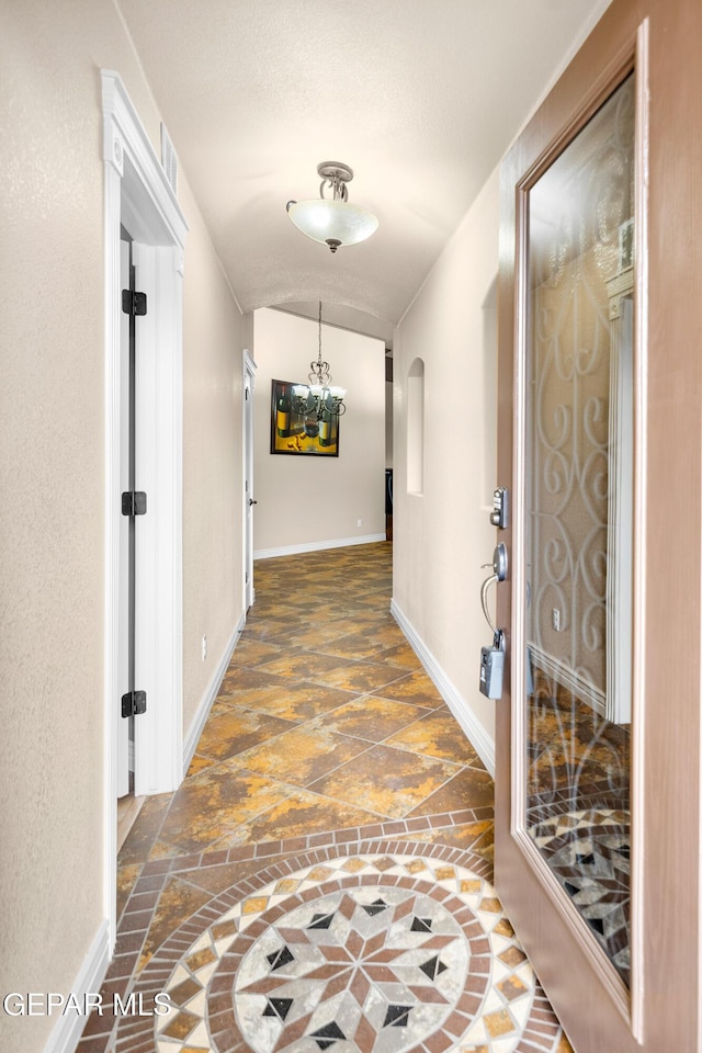 hallway with an inviting chandelier, stone finish floor, and baseboards