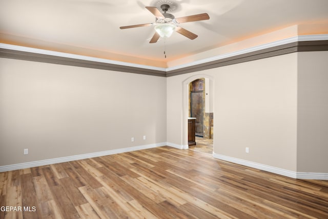 spare room with light wood-type flooring, arched walkways, baseboards, and ceiling fan