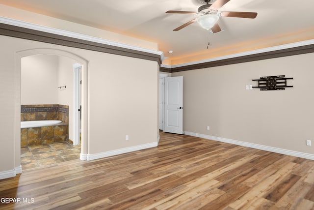 unfurnished room featuring ceiling fan, baseboards, arched walkways, and wood finished floors