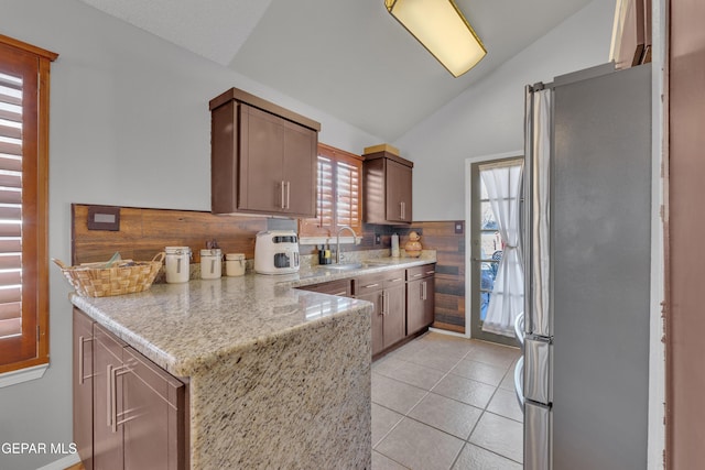 kitchen featuring a sink, freestanding refrigerator, a peninsula, light tile patterned floors, and lofted ceiling