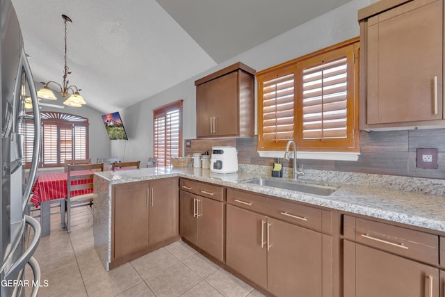 kitchen with an inviting chandelier, a peninsula, freestanding refrigerator, a sink, and vaulted ceiling