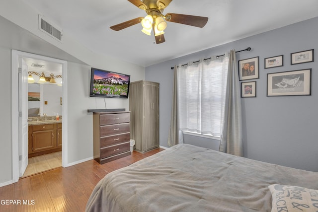 bedroom featuring wood finished floors, visible vents, baseboards, ensuite bath, and ceiling fan