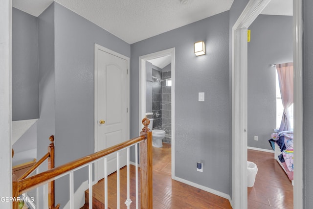 hall with wood finished floors, an upstairs landing, baseboards, and a textured ceiling