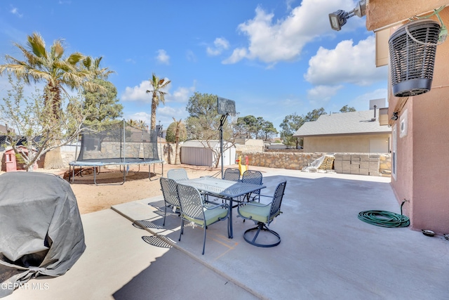 view of patio / terrace featuring a trampoline, a storage shed, an outdoor structure, outdoor dining space, and area for grilling