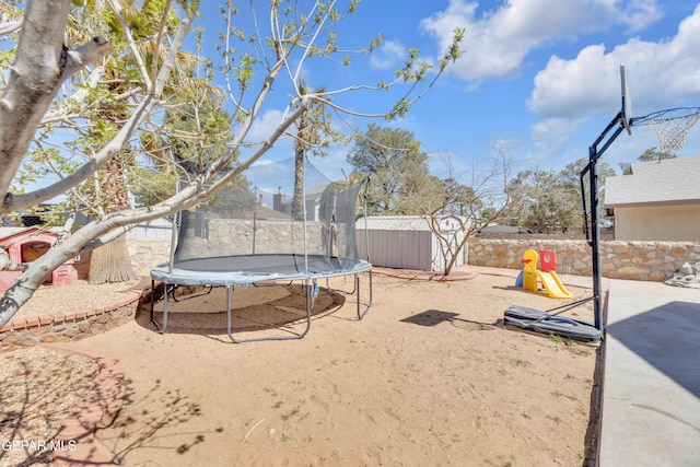 view of yard featuring a shed, an outdoor structure, a trampoline, and fence