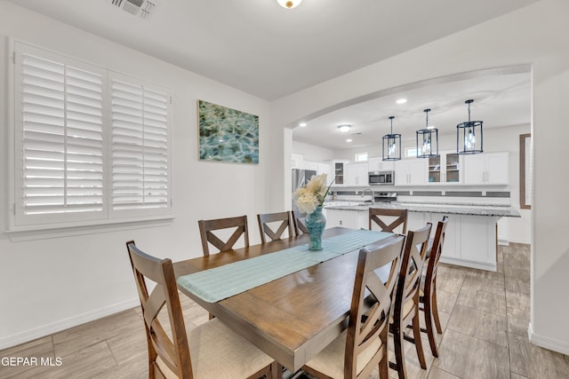 dining room featuring arched walkways, visible vents, baseboards, and wood tiled floor