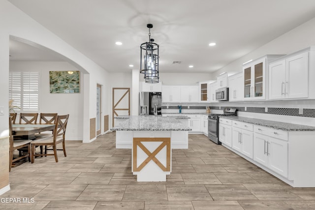 kitchen with pendant lighting, a kitchen island, arched walkways, appliances with stainless steel finishes, and white cabinets