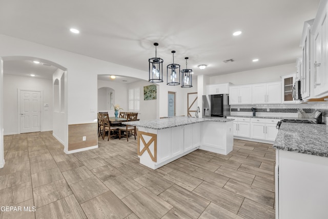 kitchen with light stone countertops, visible vents, arched walkways, appliances with stainless steel finishes, and a center island