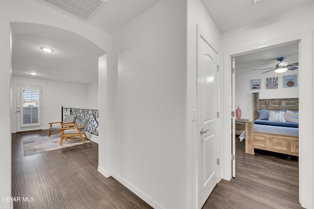 corridor featuring dark wood-style floors, visible vents, arched walkways, and baseboards