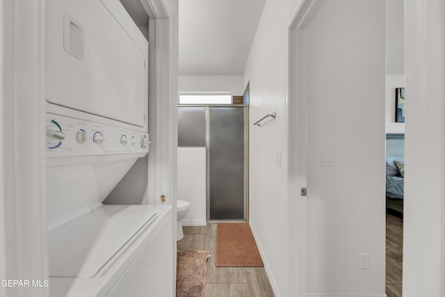 bathroom with wood finished floors, baseboards, a stall shower, stacked washer and dryer, and toilet