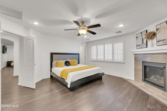 bedroom with wood finished floors, visible vents, baseboards, a fireplace, and recessed lighting