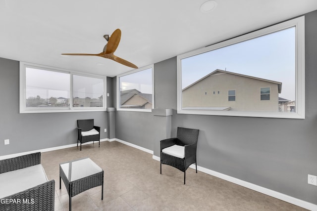 living area with baseboards and ceiling fan